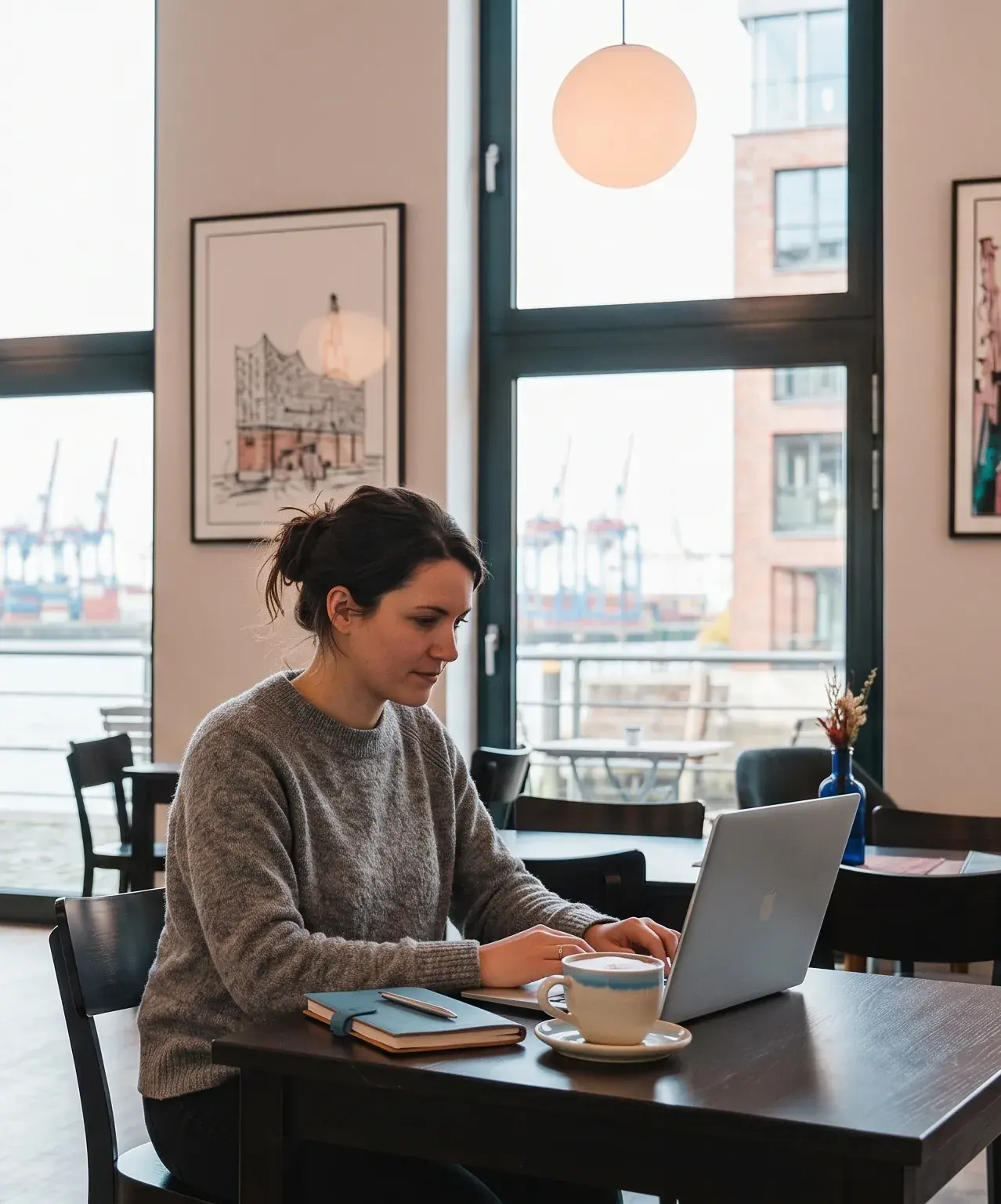 Frau arbeitet am Laptop mit Blick auf den Hamburger Hafen im Café ElbFaire